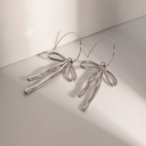 Close-up of modern silver bow earrings with fluid metal tassel design and sleek finish