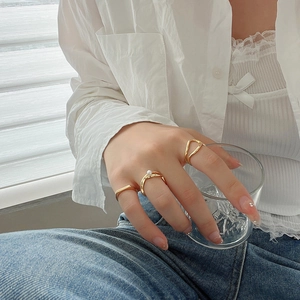 Close-up of three gold geometric rings on model hand featuring pearl and hollow designs