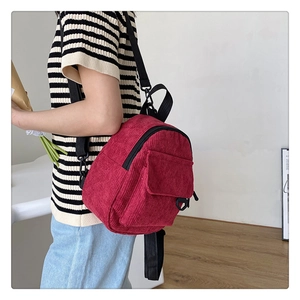 Close-up of red corduroy mini backpack with flap pocket and black straps on a model