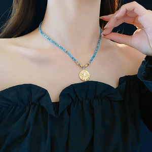 Close-up of blue beaded necklace with a golden evil eye pendant worn on a model