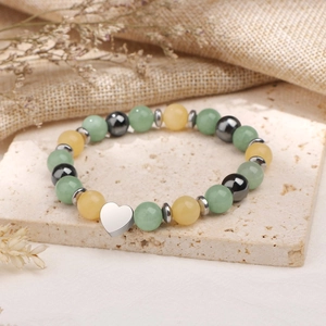 Détail du bracelet en perles avec pendentif cœur sur dalle de pierre et fleurs séchées