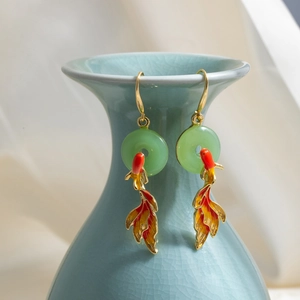 Detail of goldfish earrings with enamel finish and jade pendant on a ceramic vase