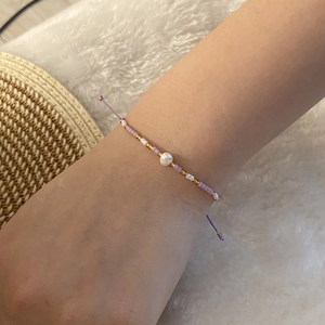 Detail of bohemian purple and gold beaded bracelet with a white pearl on a model's wrist
