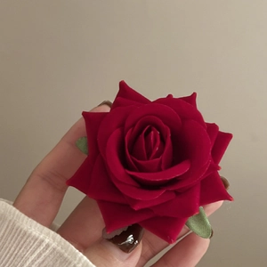 Close-up of deep red velvet rose hair clip with green fabric leaves and realistic texture