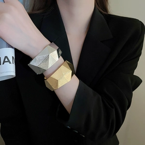 Detailansicht eines breiten Armreifs mit geometrischer Facettentextur in Gold und Silber