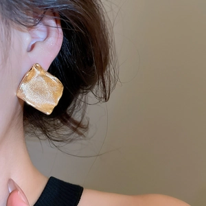 Gros plan d'un modèle portant de larges boucles d'oreilles carrées dorées à texture ondulée