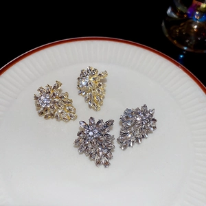 Detailed view of silver and gold leaf earrings with crystals on a ceramic tray