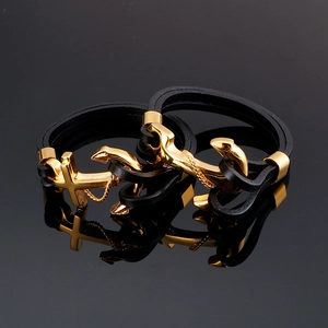 Men's leather bracelet set with gold anchor and cross charms on black reflective surface