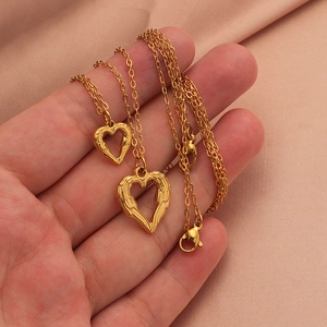 Close-up of dual gold heart pendants on stainless steel necklaces over pink silk