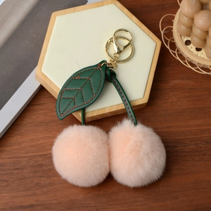 Detail of pink faux rabbit fur cherry keychain with green leather leaves and gold clasp