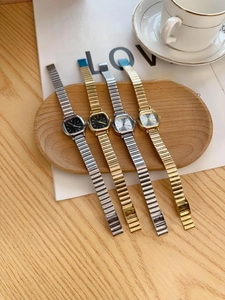Elegant small square ladies watches with gold and silver metal straps on a wooden tray
