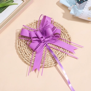 Dettaglio di fiocco in organza e raso viola su tappetino intrecciato per regali