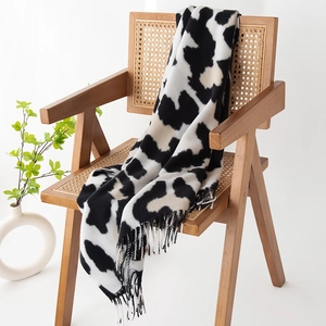 Soft black and white cow print scarf with fringe draped on a classic rattan chair