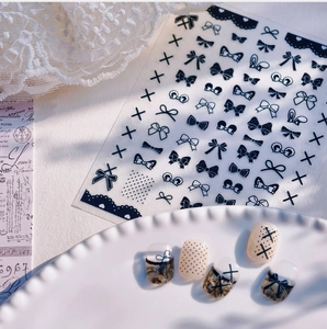 Detail of black and white bow nail stickers featuring polka dots and lace on neutral nails
