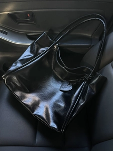 Glossy black high-capacity tote bag with heart charm on a leather car seat