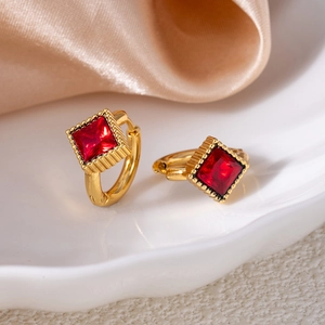 Detailed close-up of gold square ruby zircon earrings on white porcelain and silk