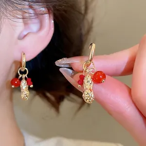 Modern gold peanut charm earrings with red crystal beads shown on a model