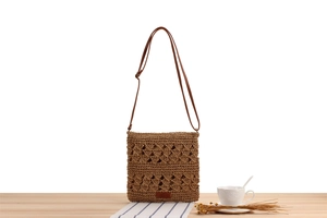 Close-up of brown hollow woven paper straw bag with leather strap on a wooden table