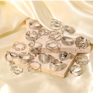 Close-up of silver-tone geometric rings with snake and heart motifs on silk and stone