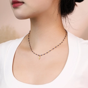 Close-up of golden stainless steel cross necklace with blue beads worn by a model