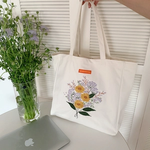 Detail of floral embroidery and orange label on a creamy white canvas tote bag