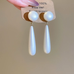 Close-up of 18k gold plated long pearl drop earrings held by hand on a card