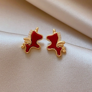 Detailed close-up of red enamel pony earrings with zircon wings on champagne silk