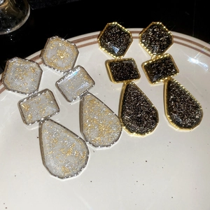 Close-up of geometric resin drop earrings in silver and gold with gold foil texture