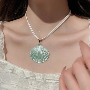 Detail of a light green shell pendant necklace worn by a model for beach vacation