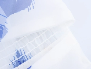 Detail des blauen Blumendrucks auf weißem Organza-Stoff mit feiner Smok-Stickerei