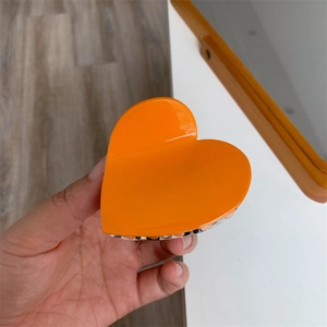 Close-up of bright orange heart-shaped hair claw clip with smooth glossy acetate finish