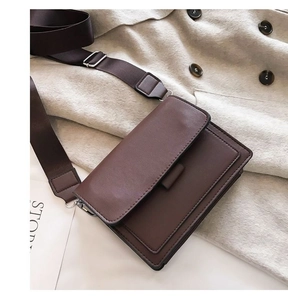 Detail of a brown leather crossbody bag with a wide adjustable strap on wool coat
