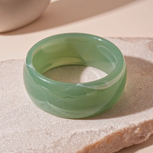 Close-up of a wide green acrylic resin ring with white marbled patterns on a stone base
