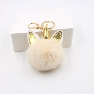 Détail d'un porte-clés licorne en peluche beige avec corne dorée et pompon doux