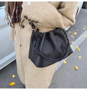 Detail of black pleated bucket bag in litchi leather carried with an autumn coat