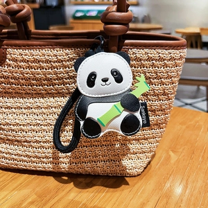 Cute panda leather bag charm with green bamboo detail on straw tote background