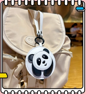 Close-up of a cute black and white leather panda charm hanging on a beige nylon backpack