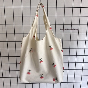 Close-up of red cherry embroidery details on a white canvas tote bag with green leaves