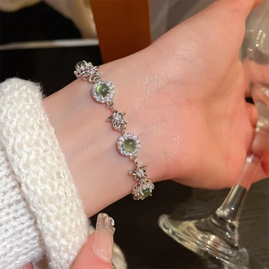 Detail view of silver floral bracelet featuring green gemstones and sparkling crystals