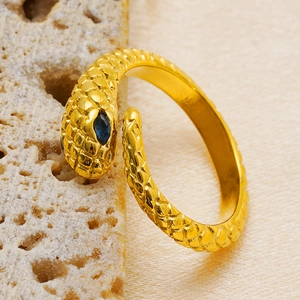 Detail view of a gold snake ring with blue gem eyes resting on a beige stone