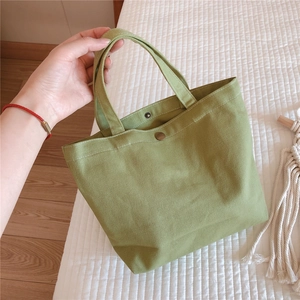 Close-up of a mini light green canvas handbag with metal snap button and sturdy handles
