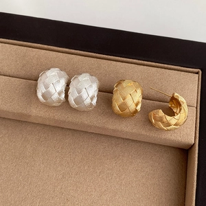Detailed view of woven texture C-shape earrings in gold and silver on velvet base