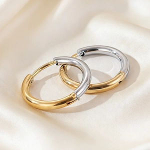 Polished two-tone gold and silver huggie earrings on light beige silk background