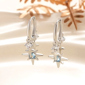 Elegant silver star earrings with light blue zircon pendants on soft beige fabric background