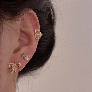 Close-up of golden heart studs and blue star ear cuffs with zircon on model ear