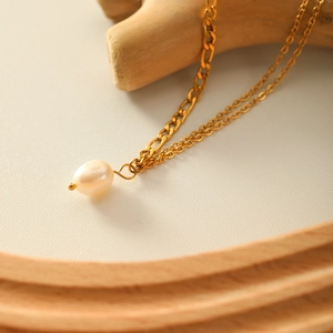 Double-layered 18K gold titanium steel necklace with a freshwater pearl on wood background