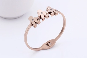 Detail of rose gold bangle featuring three human-shaped charms with tiny zircon stones