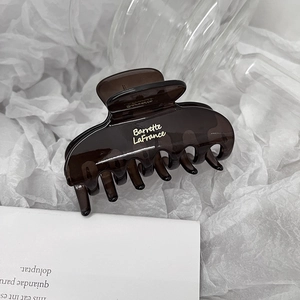 Close-up of translucent amber hair claw clip with gold lettering on white silk paper
