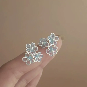Close-up of floral stud earrings with blue iridescent petals held on fingers