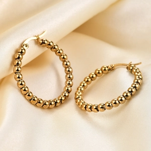 Detailed macro view of 14K gold beaded C-shape earrings on soft white silk fabric